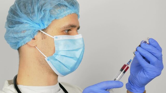 Young handsome doctor prepares for Covid-19 vaccination, prepares a syringe with a vaccine before an injection. The doctor fills a syringe with a red vaccine, preparing to inject a patient.