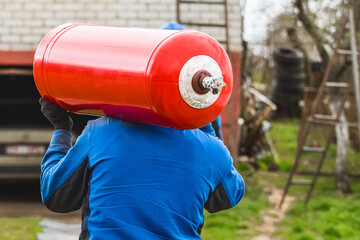 A male industrial worker walks with a gas cylinder to a gas car. Transportation and installation of...