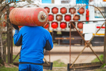 A male industrial worker walks with a gas cylinder to a gas car. Transportation and installation of a propane bottle to residential buildings