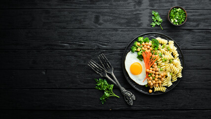 Pasta with vegetables and fried egg on a black stone plate. Bowl Buddha. Top view. Free space for text.
