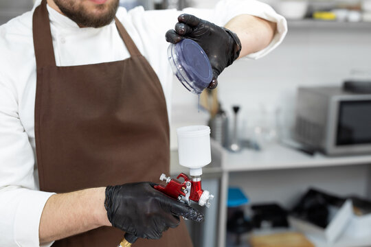 Male pastry chef pours colored chocolate into an airbrush, spray gun