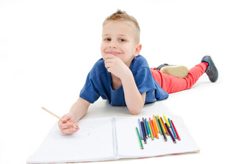 Young boy lying on floor with pencils on a sketch book with a look of concentration, close up view. Isolated on white background
