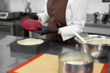 Young pastry chef puts a berry filling in a mousse cake. Preparation of cake, dessert in a professional kitchen.