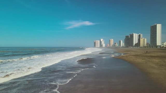 Sea waves crashing against the shore, Aerial view of the ocean in Iquique, Chile. South America. drone shot of dog walking on the beach. Aerial view of a wide wild sandy beach by the city skyscrapers