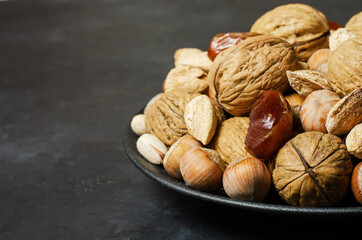 Nuts and dates in a plate on a dark concrete background. Source of vegetable protein and vitamins.