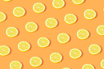 Minimal fruit pattern made with yellow lemon slices with sunlight shadow on bright orange background. Creative food concept.