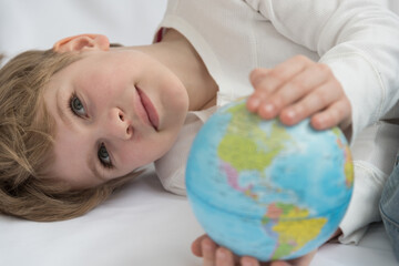 The child dreamily examines the globe. Travel yearning concept. Closed borders and quarantine. A European-looking child dreams of travel