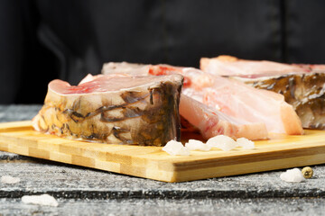 slices of fresh carp seasoned with salt and pepper on a cutting board against a black background.