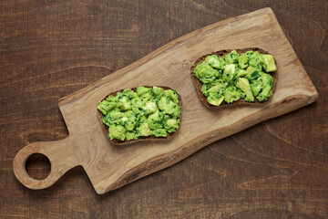 Two sandwiches with avocado guacamole spreaded on bread slice. Olive wood cutting board, flat lay.