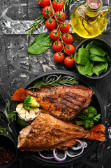 Baked red fish perch with vegetables on a black stone plate. Top view. Free space for your text.