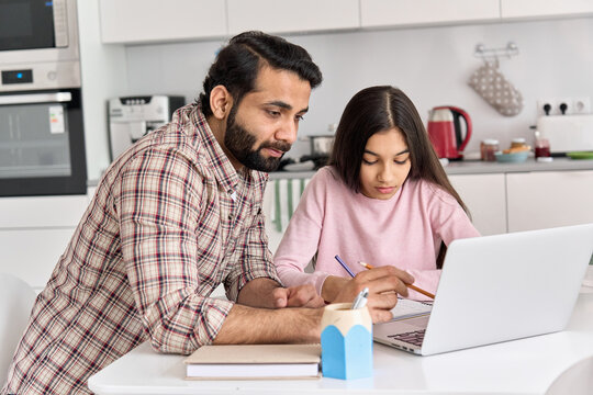 Young indian father helping school child teen daughter studying online at home. Dad and kid girl elearning having virtual class on laptop, studying remote homeschool lesson on computer together.