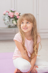 Naklejka premium Full length front view smiling preschool girl sitting on on yoga mat.