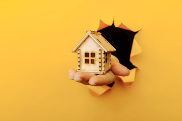 Hand with a wooden house model through a yellow paper hole