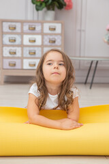 Full length front view cute playful little girl sitting on yoga mat looking