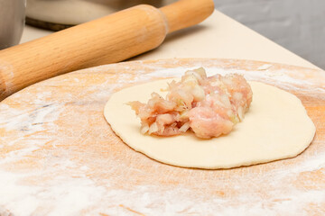 Meat pie in the process of preparation sprinkled with flour on a cutting board.