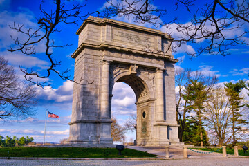Fototapeta na wymiar The National Memorial Arch stands with the American Flag blowing in the wind to the left at Valley Forge National Park in Pennsylvania.