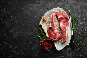 Fresh raw veal steak on the bone with rosemary and spices. On a black stone background. Top view. - obrazy, fototapety, plakaty