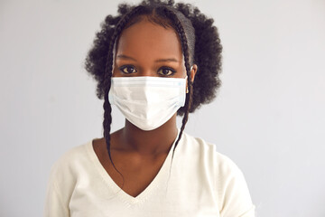 Close up headshot of young responsible citizen wearing disposable surgical face mask. Confident black lady in protective mask isolated on light gray background. Covid 19 safety in coronavirus pandemic