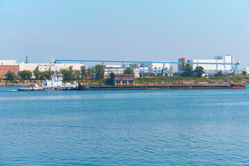 towboat pushes dry bulk cargo barge on the river against the backdrop of an industrial landscape on...