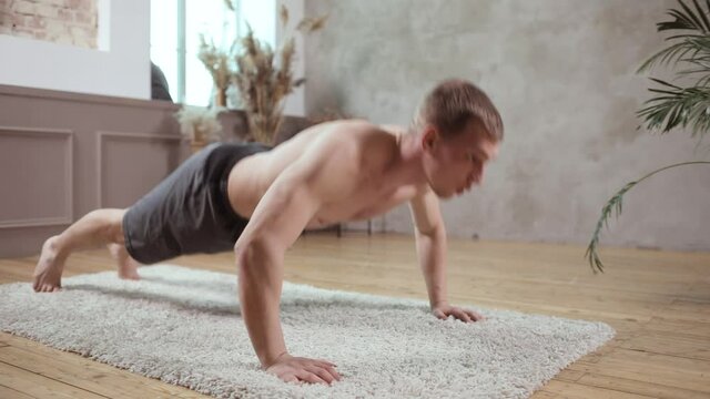 A young european man works out, doing push-ups on a wooden floor while lying on a mat. Close-up side view. Healthy lifestyle and sport concept.