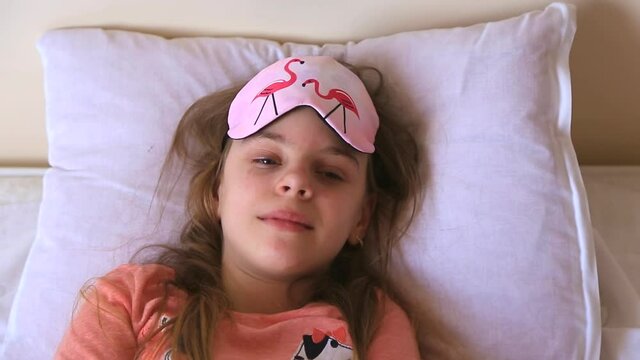 Beautiful young girl in pink pajamas and a sleep mask on her eyes. girl woke up in the morning, the concept of a happy start to the day