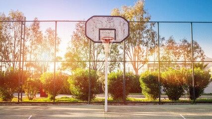 Empty basketball court with high backboard behind metal fence