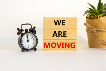 We are moving symbol. Wooden blocks with words 'We are moving'. Beautiful white background, black alarm clock, house plant. Business, we are moving concept, copy space.