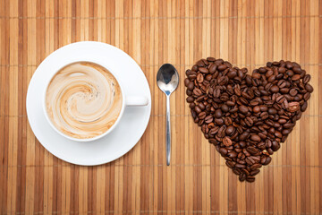 Heart of coffee beans with a cup of coffee on a brown background High quality photo. Top view