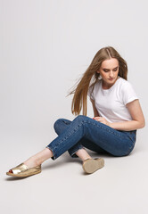 young beautiful woman in a white t-shirt and jeans on a white background. Young woman sit on white background. Photo concept for advertisements of clothes and shoes