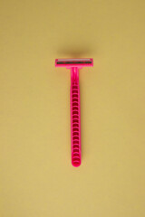 Pink one-time female razor on a yellow background. Bright colors, minimalism. Smooth legs, daily self-care