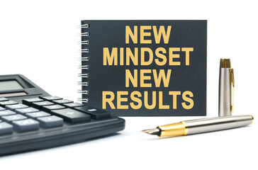 On a white background, there is a calculator, a pen and a black notebook with the inscription - NEW MINDSET NEW RESULTS