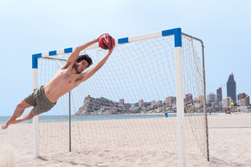 Diagonal perspective of a soccer goalkeeper on the beach stopping a ball.