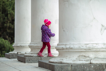 Fototapeta na wymiar A Caucasian four-year-old girl in purple and pink clothes walks in the park