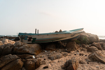Mała łódź rybacka wyrzucona na skały na tle wybrzeża i nieba. © insomniafoto