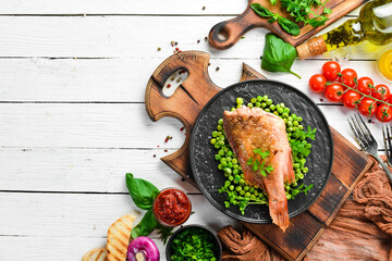 Baked sea red perch with green peas on a black stone plate. Top view. Free copy space.
