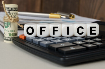 There are cubes on the calculator that say - OFFICE. Nearby out of focus - dollars, notebook and pen