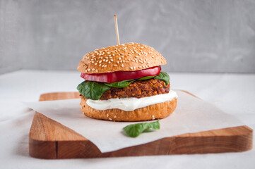 Vegan burger made with red beans, red pepper, spinach, white yoghurt and fresh salad leaves and cut vegetables at the background.