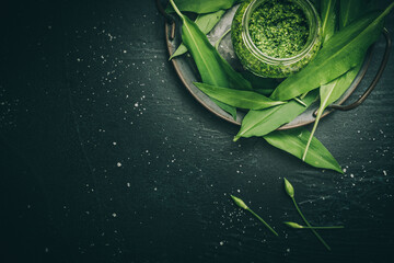 Homemade wild garlic pesto and wild garlic leaves on a metal tray on black background with copy...