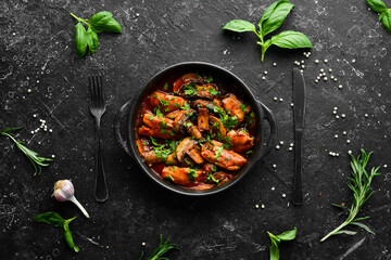 Baked mushrooms with chicken fillet in tomato sauce. In a black stone plate. Top view.