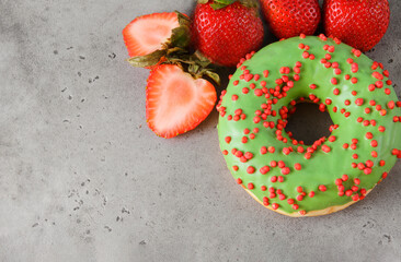 1 green donut,  fresh red strawberries on a gray