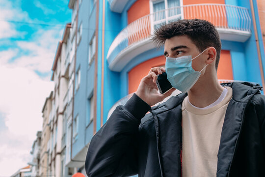 Young Man With Mask Talking On Mobile Phone In The Street