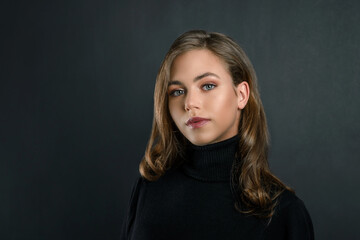 beautiful young blonde girl close up in black clothes on a black background. portrait of a...