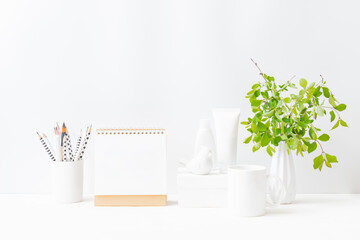 Home interior with decor elements. Mockup white desk calendar and branches with green leaves in a vase on a light background
