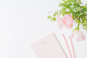 Flat lay home office desk with pink tulips in a vase, notebook on a light background