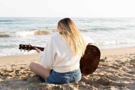 Young beautiful woman playing acoustic guitar on beach at sunset.Unrecognizable female enjoying summer holidays outdoor in sandy beach.