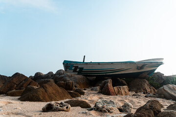 Mała łódź rybacka wyrzucona na skały na tle wybrzeża i nieba.