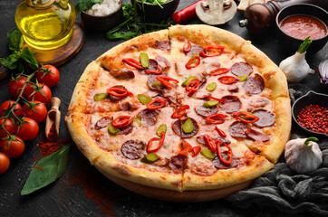 Spicy pizza with sausages and chili peppers. On a black stone background. Free space for text.