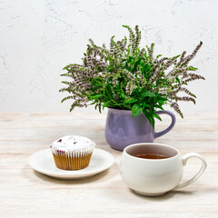Cupcake and coffee tea mug on a background of mint flowers on a white wooden table. Tea party with a cupcake.