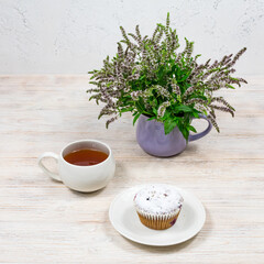 Cupcake and coffee tea mug on a background of mint flowers on a white wooden table. Tea party with a cupcake.