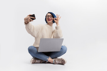 A woman sitting on the floor, holding a laptop and taking selfie